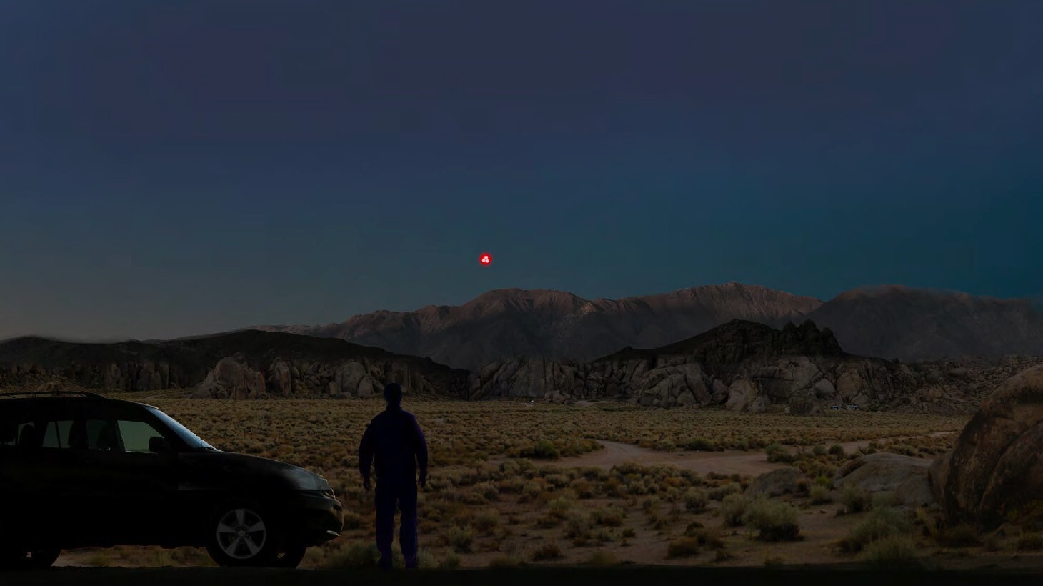A digital rendering of a person standing in a desert landscape at night, with several red light sources visible in the sky.