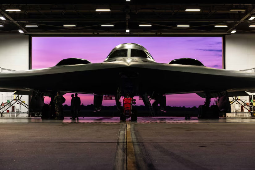 A B-2 Spirit aircraft sits in front of a purple screen a hangar. 